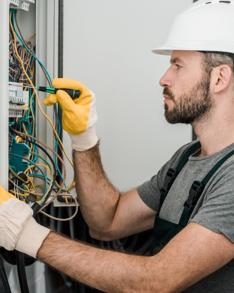 side-view-of-handsome-bearded-electrician-repairing-electrical-box-and-using-screwdriver-in-corridor.jpg